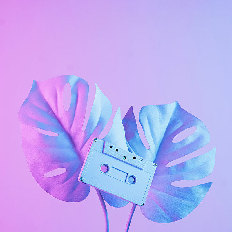 Cinta de radio casette retro sobre dos preciosas hojas de palma con un fondo de neon en tonos violeta.