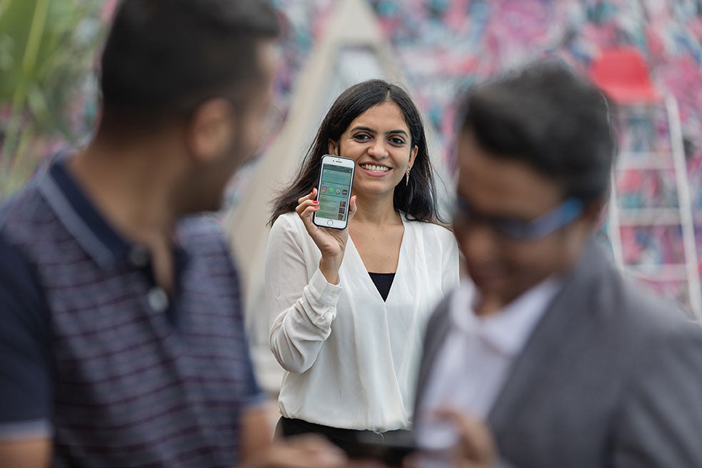 Mujer sonriente levanta su teléfono movil y muestra a dos hombres que desde su celular tiene controlada su red de marketing de afiliados.